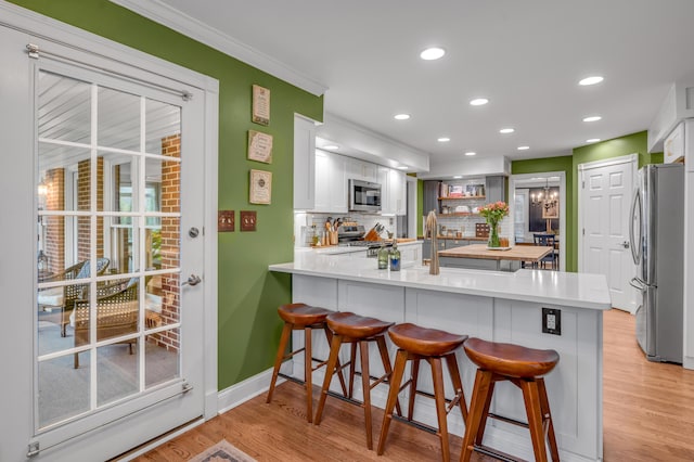 kitchen featuring a breakfast bar, tasteful backsplash, white cabinets, kitchen peninsula, and stainless steel appliances