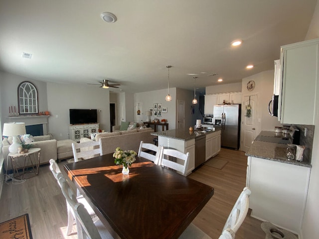 dining room featuring a fireplace, ceiling fan, light hardwood / wood-style flooring, and sink