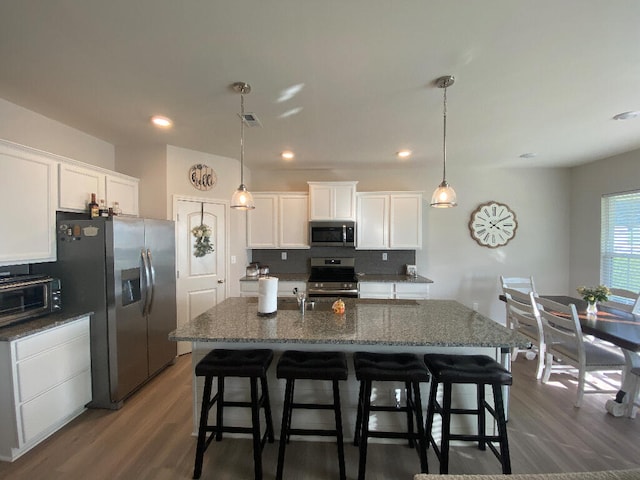 kitchen with white cabinetry, a kitchen island with sink, dark hardwood / wood-style floors, and appliances with stainless steel finishes