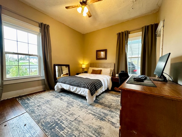 bedroom featuring a textured ceiling, ceiling fan, dark wood-type flooring, and multiple windows