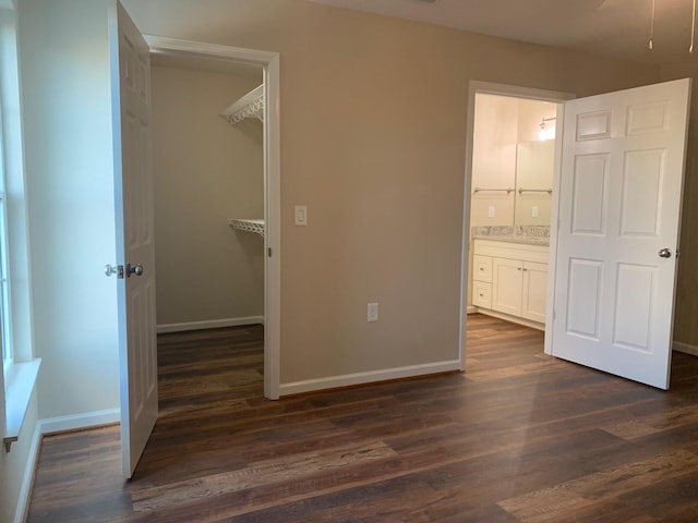 unfurnished bedroom featuring connected bathroom, a walk in closet, and dark hardwood / wood-style flooring