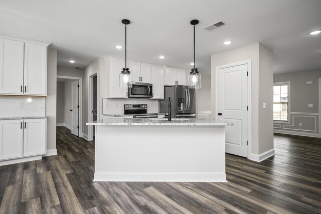 kitchen with light stone counters, an island with sink, pendant lighting, stainless steel appliances, and white cabinets