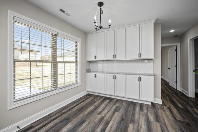 kitchen with decorative light fixtures, dark hardwood / wood-style floors, white cabinets, light stone countertops, and backsplash