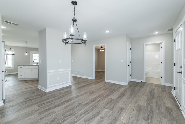 unfurnished dining area featuring ceiling fan with notable chandelier and light wood-type flooring