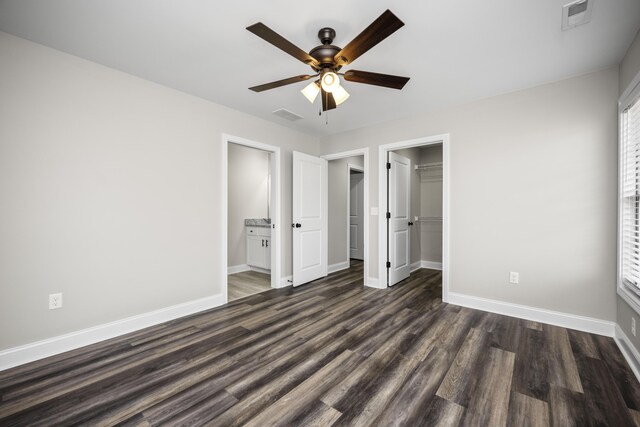 unfurnished bedroom featuring ensuite bath, dark wood-type flooring, ceiling fan, a walk in closet, and a closet