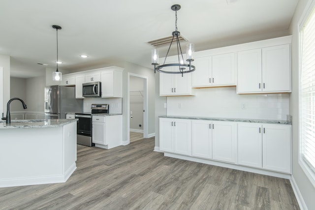 kitchen featuring white cabinets, appliances with stainless steel finishes, light wood-type flooring, and light stone counters