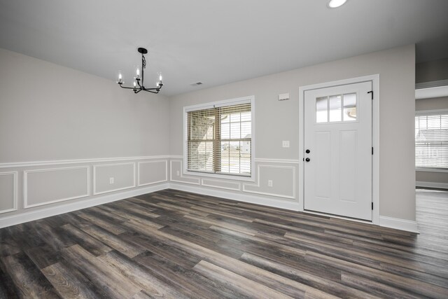 foyer entrance with dark hardwood / wood-style flooring, a wealth of natural light, and an inviting chandelier