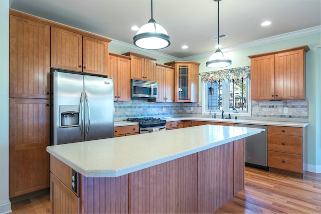 kitchen featuring appliances with stainless steel finishes, ornamental molding, light hardwood / wood-style floors, a kitchen island, and hanging light fixtures