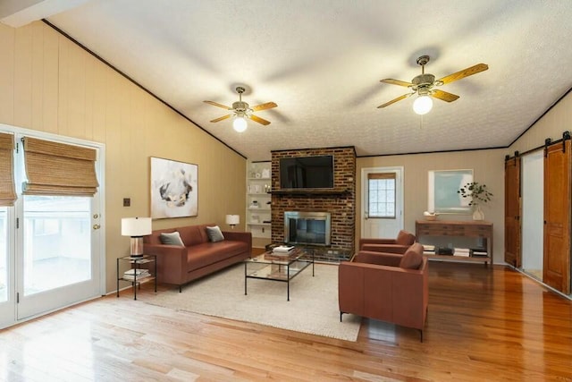 living room featuring lofted ceiling, wood-type flooring, a barn door, and ceiling fan