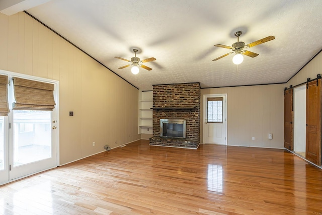 unfurnished living room featuring ceiling fan, a fireplace, a textured ceiling, a barn door, and light wood-type flooring