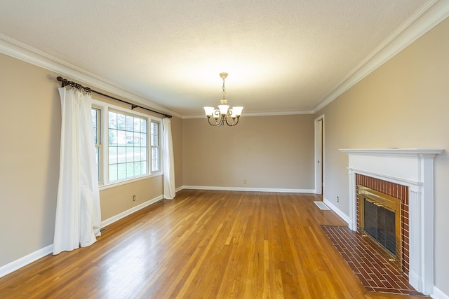 unfurnished living room featuring crown molding, an inviting chandelier, hardwood / wood-style floors, a fireplace, and a textured ceiling