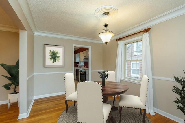 dining area featuring ornamental molding, sink, light hardwood / wood-style flooring, and a textured ceiling