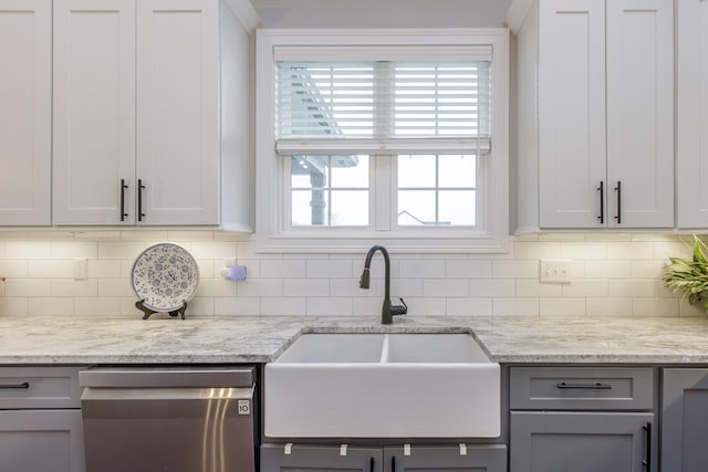 kitchen with stainless steel dishwasher, light stone counters, and sink