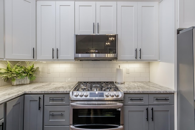 kitchen featuring appliances with stainless steel finishes, tasteful backsplash, light stone counters, gray cabinetry, and white cabinetry