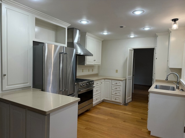 kitchen with sink, wall chimney exhaust hood, kitchen peninsula, high quality appliances, and white cabinets