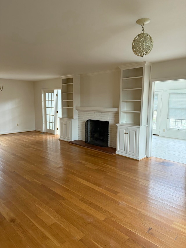 unfurnished living room featuring a fireplace, light hardwood / wood-style flooring, and built in shelves