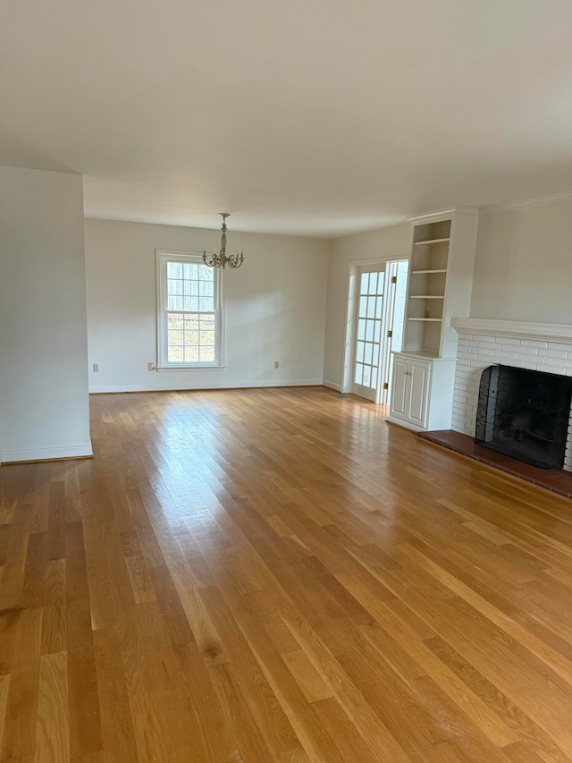 unfurnished living room with a fireplace, a chandelier, and light hardwood / wood-style flooring