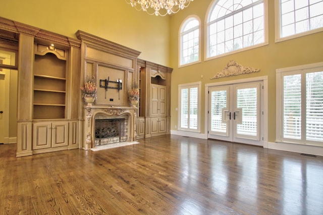 unfurnished living room featuring built in shelves, a high end fireplace, dark hardwood / wood-style floors, and a notable chandelier