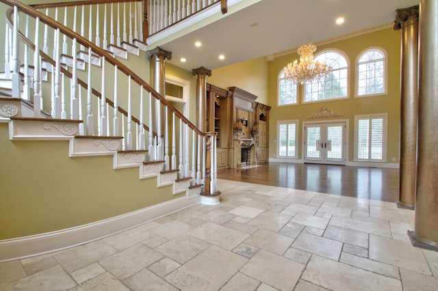 entryway featuring a towering ceiling, french doors, a chandelier, and ornate columns