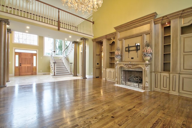 unfurnished living room featuring a fireplace, hardwood / wood-style floors, a towering ceiling, and built in shelves