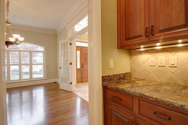 interior space featuring crown molding, a chandelier, decorative light fixtures, decorative backsplash, and light wood-type flooring