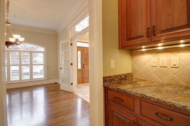 interior space with pendant lighting, tasteful backsplash, ornamental molding, a notable chandelier, and light hardwood / wood-style flooring