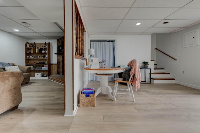 dining room featuring light hardwood / wood-style flooring, a drop ceiling, and a brick fireplace
