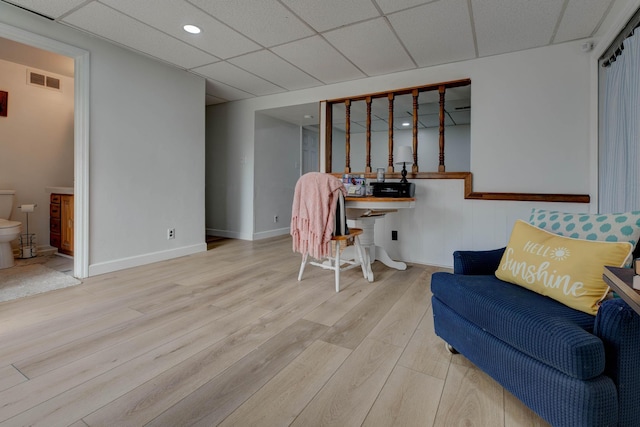 living area with a paneled ceiling and light hardwood / wood-style flooring