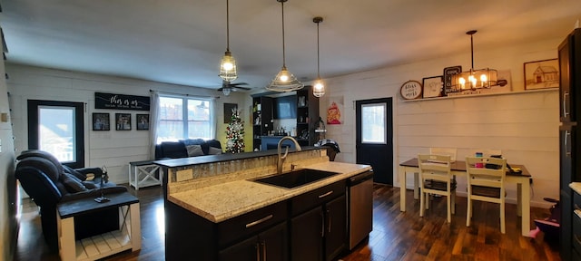 kitchen featuring a center island with sink, sink, hanging light fixtures, dark hardwood / wood-style floors, and light stone counters