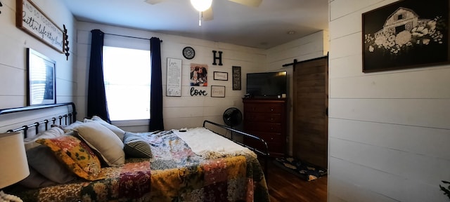 bedroom with a barn door, hardwood / wood-style flooring, multiple windows, and ceiling fan