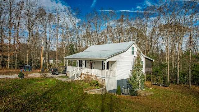 view of side of property featuring covered porch, a trampoline, cooling unit, and a lawn