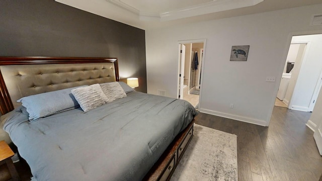 bedroom featuring a raised ceiling, dark wood-type flooring, and ensuite bath