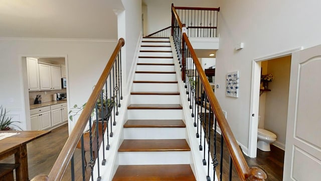 staircase with crown molding, a towering ceiling, and hardwood / wood-style flooring