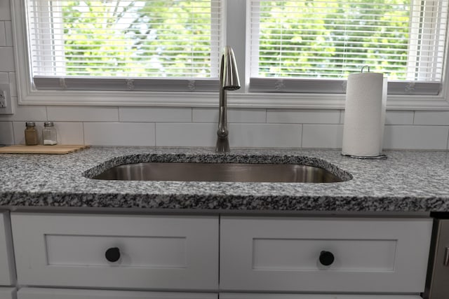 details featuring backsplash, white cabinetry, sink, and dark stone counters