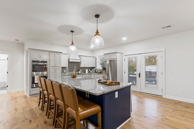 kitchen with a breakfast bar area, stainless steel appliances, visible vents, light wood-style floors, and tasteful backsplash