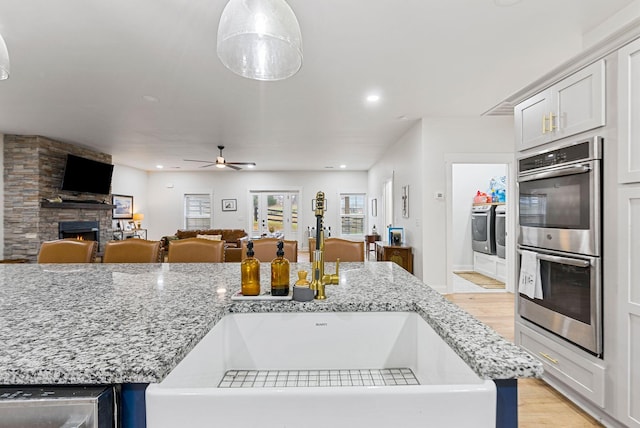 kitchen with a fireplace, double oven, a sink, separate washer and dryer, and light wood-type flooring