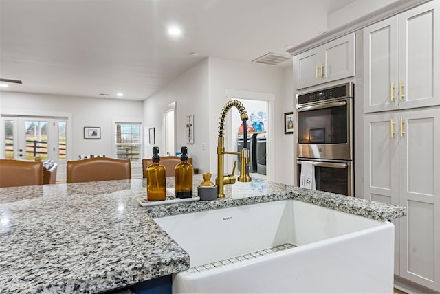 kitchen with light stone counters, recessed lighting, visible vents, stainless steel double oven, and a sink