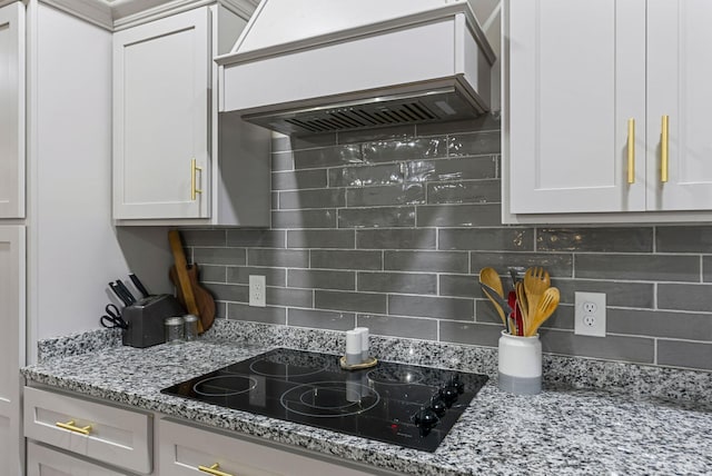 kitchen with backsplash, white cabinetry, light stone countertops, premium range hood, and black electric cooktop