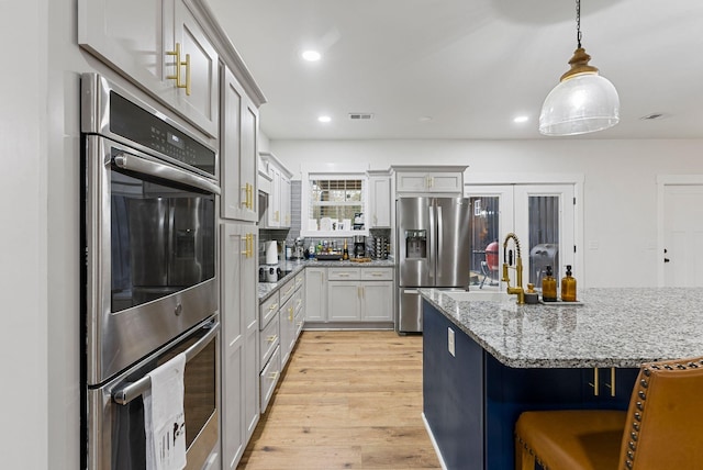 kitchen featuring light wood finished floors, visible vents, appliances with stainless steel finishes, a breakfast bar area, and pendant lighting