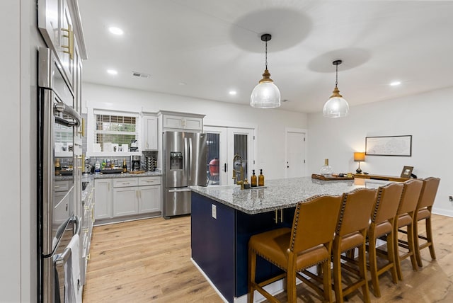 kitchen with visible vents, stainless steel fridge with ice dispenser, a kitchen island, light stone counters, and light wood-style floors