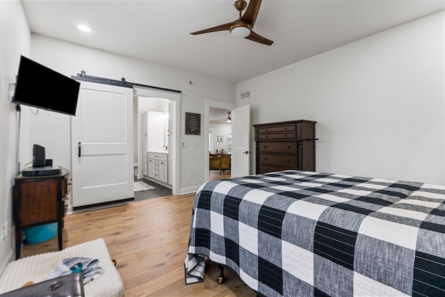 bedroom with ceiling fan, ensuite bathroom, a barn door, baseboards, and light wood finished floors