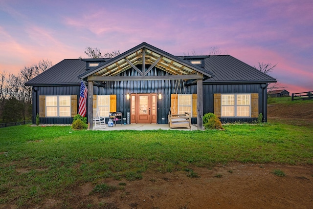 back of property at dusk featuring a patio, a lawn, board and batten siding, a standing seam roof, and metal roof