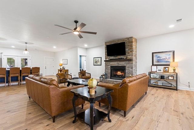 living room featuring ceiling fan, a stone fireplace, light wood-type flooring, and recessed lighting