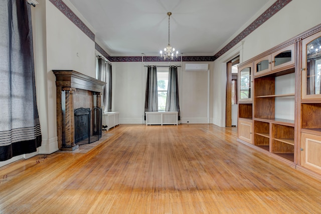 unfurnished living room with radiator, a wall unit AC, hardwood / wood-style floors, a chandelier, and a tiled fireplace