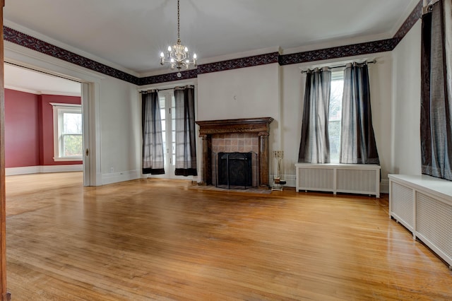 unfurnished living room featuring radiator heating unit, crown molding, a tile fireplace, and light hardwood / wood-style flooring