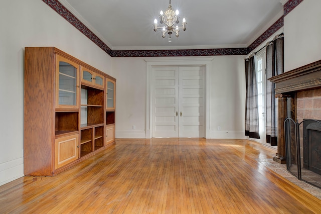 unfurnished living room with a brick fireplace, light wood-type flooring, an inviting chandelier, and crown molding