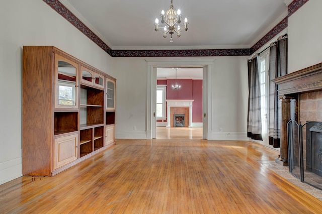 unfurnished living room with a tile fireplace, hardwood / wood-style floors, crown molding, and a notable chandelier