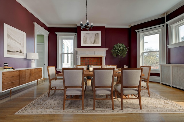 dining area featuring a tile fireplace, crown molding, light hardwood / wood-style flooring, and an inviting chandelier