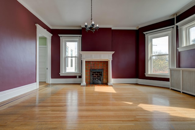 unfurnished living room with a tile fireplace, crown molding, light hardwood / wood-style floors, and an inviting chandelier