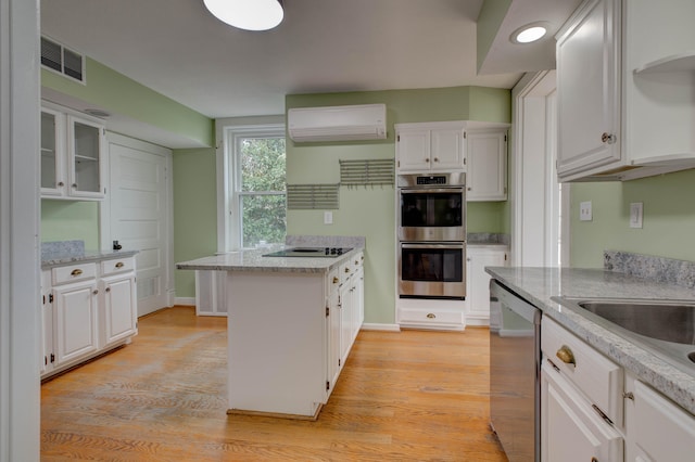 kitchen with white cabinets, light wood-type flooring, an AC wall unit, and appliances with stainless steel finishes